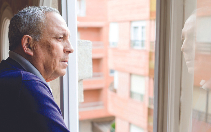 Man looking out his apartment window with his reflection in the window